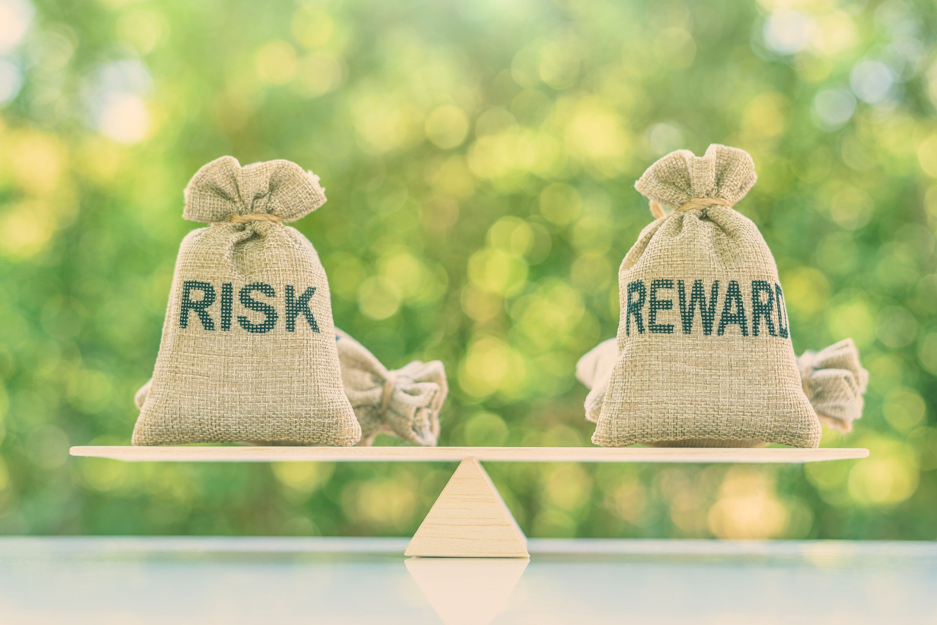 Risk reward ratio / risk management concept : Risk and reward bags on a basic balance scale in equal position, depicts investors use a risk reward ratio to compare the expected return of an investment