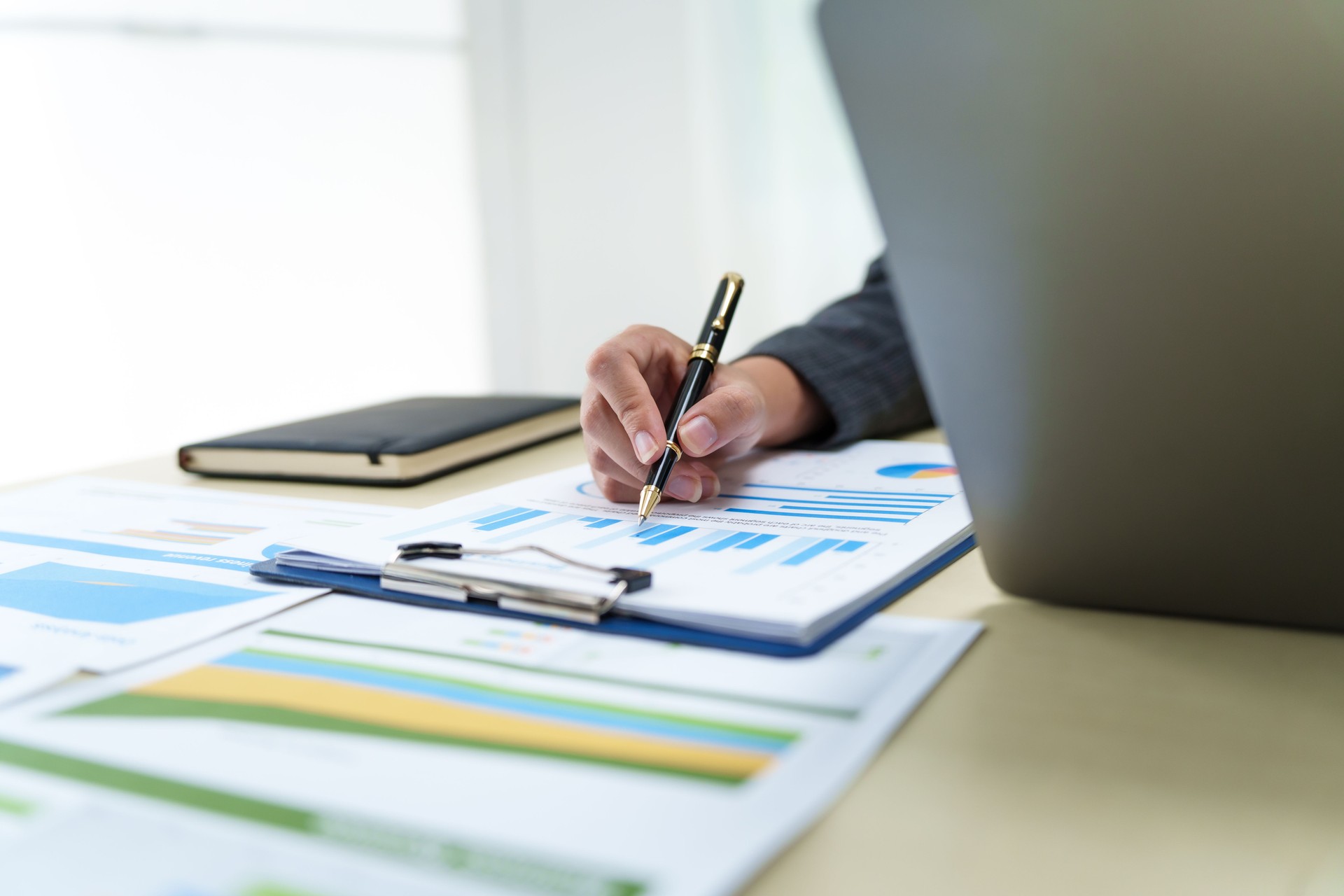 A businesswoman in a grey suit works from home, specializing in policy and planning analysis, managing financial tasks at desk with a whiteboard and expertise in accounting and financial services.