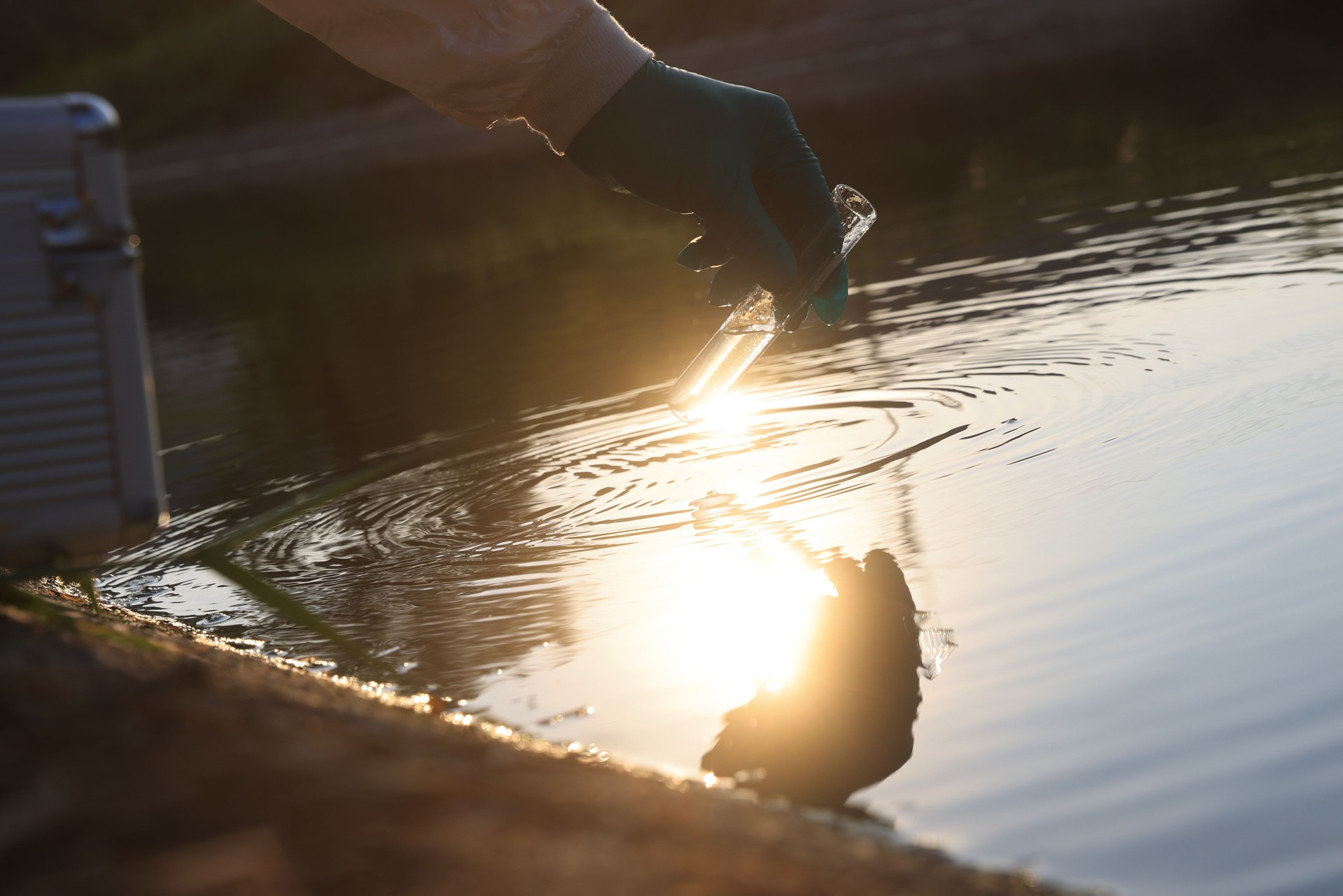 Close-up scientist hand with white PPE suit and nitrile gloves collect sample wastewater into to flask for laboratory water analysis, industrial and environmental concept